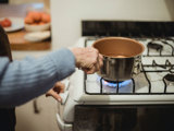 Person holding a pot of boiling water on a stove